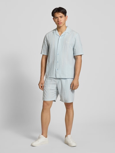 Männermodel trägt Leinenshorts mit Logo-Stitching von REVIEW, hellblauer Baumwoll-Leinen-Mix, Regular Fit, seitliche Taschen, Ganzkörperansicht von vorne.