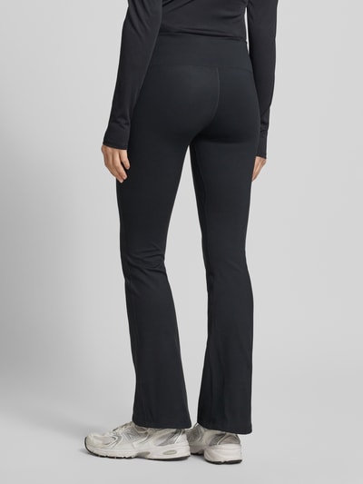 Frauenmodel trägt Flared Cut Leggings mit Logo von NIKE TRAINING, schwarz, elastischer Bund, Material-Mix, Ganzkörperansicht Rückansicht.