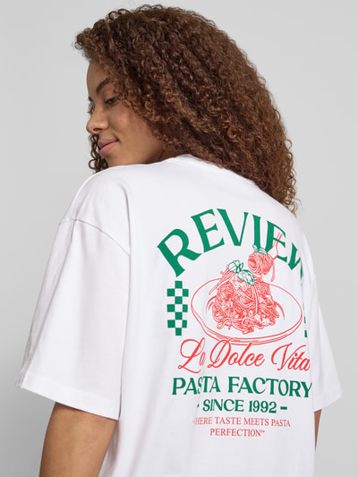 Frauenmodel trägt T-Shirt mit rückseitigem Motiv-Print von REVIEW in Weiß mit Oversized-Schnitt, Reine Baumwolle, Rundhalsausschnitt, Rückenlänge 68 cm, Nahaufnahme Rückansicht.