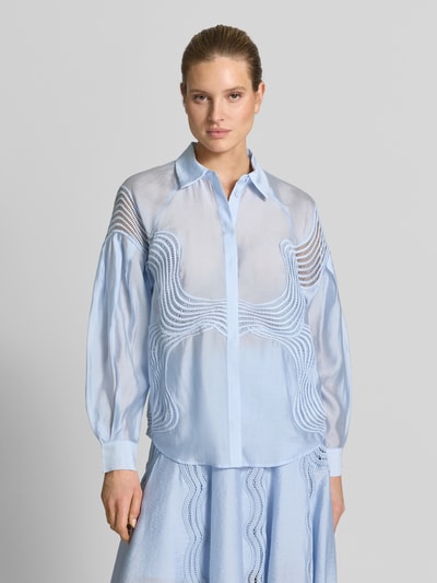 Modelka kobieca ma na sobie Regular Fit Bluse mit verdeckter Knopfleiste Modell 'MOLLY' od Copenhagen Muse, jasnoniebieska, krój regular fit, kołnierz koszulowy, długość tyłu 67 cm, długość rękawa 76 cm, tkanina lekko prześwitująca, przód zdobiony wzorem, widok całego przodu górnej części ciała.