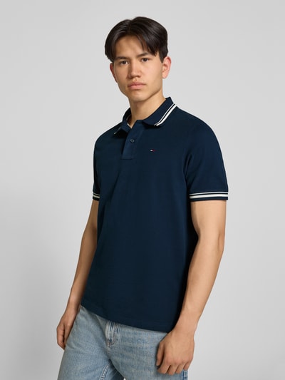 Männermodel trägt Regular Fit Poloshirt aus reiner Baumwolle von Tommy Jeans, Optik: Unifarben, Logo-Stitching, Ganzkörperansicht von vorne.