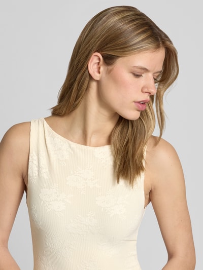 Modelka nosi Slim Fit Top mit floralem Allover-Stitching Modell 'Jacquard' od Gina Tricot, elastyczna mieszanka materiałów, krój slim fit, długość tyłu w rozmiarze S: 47 cm, kremowy kolor, wyraźna tekstura, kwiatowy haft; zbliżenie na górę ciała z przodu.