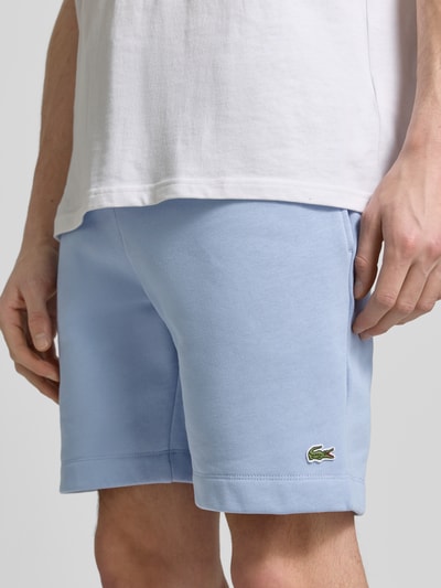 Männermodel trägt Regular Fit Sweatshorts aus Baumwoll-Mix von Lacoste in uni hellblau, elastischer Bund, seitliche zakken, label patch, sweat materiaal, Ganzkörperansicht von vorne.