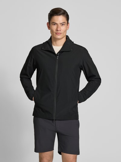 Männermodel trägt Regular Fit Jacke mit Kapuze von SCANDINAVIAN EDITION in Schwarz, glatte Struktur, Zweiwege-Reißverschluss, Eingrifftaschen, Ganzkörperansicht von vorne.