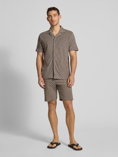 Mężczyznamodel nosi Regular Fit Shorts mit Label-Patch von Lindbergh z bawełnianej mieszanki, kolor beżowy, kieszenie boczne i tylna, szerokość w rozmiarze M: 45 cm, długość nogawki od wewnątrz: 22 cm, krój regular fit, widok całej sylwetki z przodu.