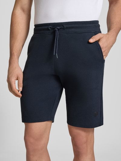Männermodel trägt Straight Fit Shorts mit Logo-Stitching Modell 'Fillip' von Blend aus Reine Baumwolle mit Strukturmuster, Eingrifftaschen, elastischer Bund mit Tunnelzug, dunkelblaue Farbe, Nahaufnahme Oberkörper.