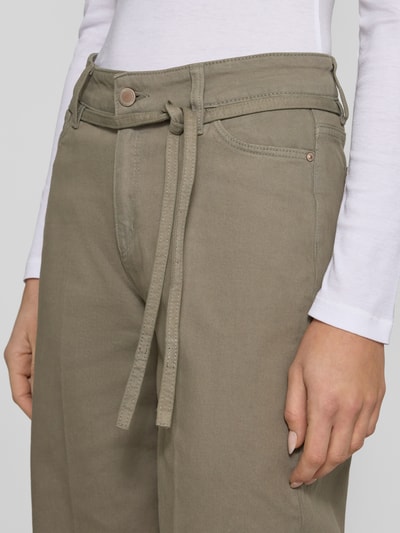 Kobieta nosi Wide Fit Jeans mit Bügelfalten od Christian Berg Woman w kolorze khaki, bawełniany elastyczny materiał, pięć kieszeni, zdejmowany pasek, guziki i zamek, Szerokość w rozmiarze 36/32: 107 cm, długość nogawki: 77 cm, zbliżenie na górną część jeansów.