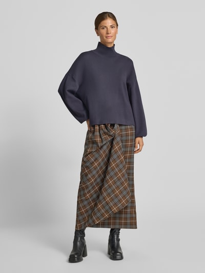 Frauenmodel trägt Strickpullover aus Viskose-Mix Modell 'Mercy East' von MSCH Copenhagen in Dunkelblau mit Stehkragen, Relaxed Fit, kombiniert mit karierter Maxirock, Ganzkörperansicht von vorne.