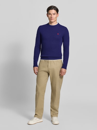 Männermodel trägt Slim Fit Strickpullover aus reiner Wolle mit Label-Stitching von MCNEAL in Blau, kombiniert mit heller Hose, Ganzkörperansicht von vorne. Rückenlänge 66 cm, Ärmellänge 69 cm, gerippte Abschlüsse.