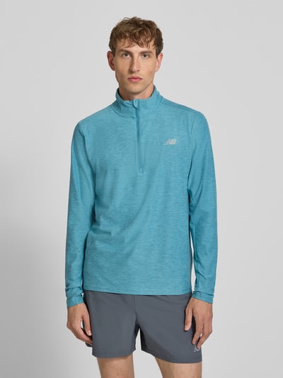 Męski model nosi Regular Fit Sweatshirt mit Troyer-Kragen von New Balance, elastyczna mieszanka materiałów, krój regular fit, nadruk z logo, długość tyłu w rozmiarze M: 69 cm, widok całej sylwetki z przodu.