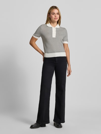 Frauenmodel trägt Poloshirt mit gerippten Abschlüssen von MANGO, kurzärmelig, gerade Passform, schwarz-weiß gestreift, Ganzkörperansicht von vorne.
