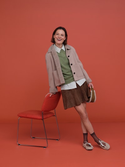 Frauenmodel trägt Regular Fit A-Linien Mini-Rock aus Veloursleder von HUGO in Braun, kombiniert mit grüner Strickjacke, Ganzkörperansicht von vorne, Damen Mini-Rock von HUGO.