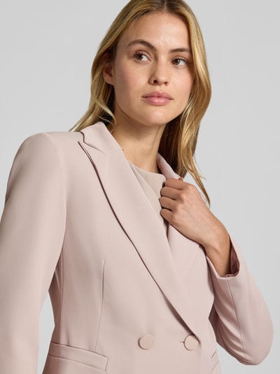 Vrouwenmodel draagt blazer met dubbele knoopsluiting van Rinascimento in lichtroze, Reverskraag, getailleerde pasvorm, paspelzakken, ruglengte maat S: 64 cm, close-up bovenlichaam.