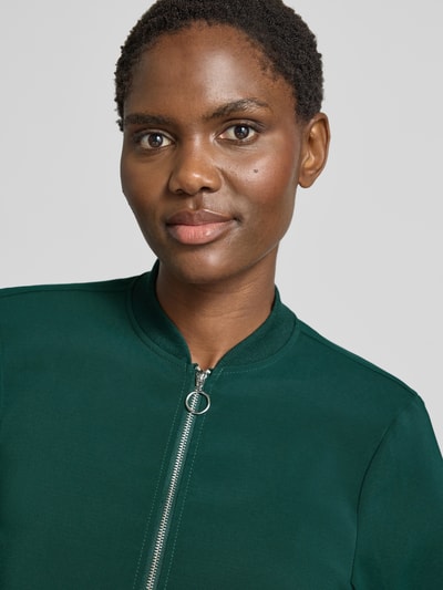 Frauenmodel trägt Regular Fit Blouson mit Reißverschluss-Detail von VERO MODA in dunklem Grün, glatte Struktur, Nahaufnahme Oberkörper. Damen Bomberjacke / Blouson