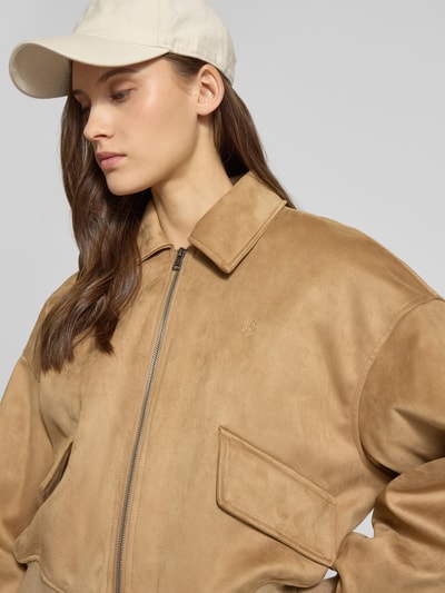Modelka nosi Regular Fit Bomberjacke mit Umlegekragen od Guess Jeans, brązowy kolor, zamek, elastyczne wykończenia, krój regular fit, zbliżenie na górną część ciała