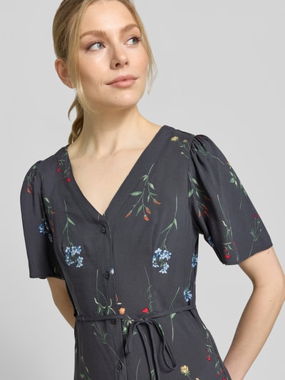 Frauenmodel trägt Leicht ausgestelltes Minikleid aus reiner Viskose Modell 'ALBA' von Vero Moda, Optik: Unifarben, Passform: Leicht ausgestellt, Länge: Mini, Ausschnitt: V-Ausschnitt, Details: Taillengürtel, Verschluss: Knopfleiste, Ärmelform: Kurzarm, weite Ärmel, Material: Reine Viskose, florales Muster, glatte Struktur, Nahaufnahme Oberkörper.