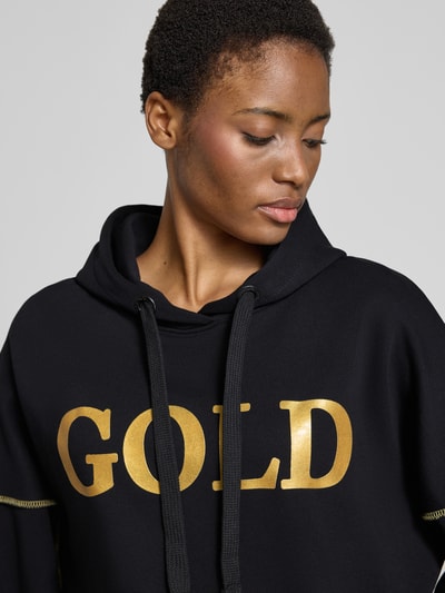 Frauenmodel trägt Oversized Hoodie aus reiner Baumwolle Modell 'Silver and Gold' von miss goodlife mit Statement-Print, Nahaufnahme Oberkörper.