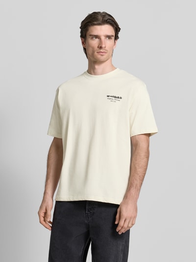 Mężczyzna prezentuje T-Shirt mit Label-Print Modell 'Baine' von WOODBIRD z czystej bawełny, krój regular fit, kremowy, widok całej sylwetki z przodu.