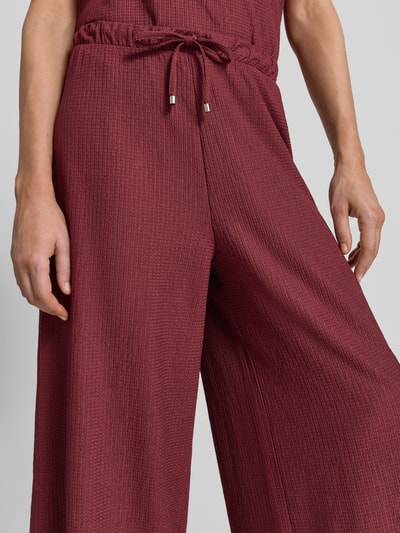 Frauenmodel trägt Loose Fit Hose in Crinkle-Optik von s.Oliver RED LABEL in dunklem Rot, feine Struktur, Nahaufnahme Oberkörper.