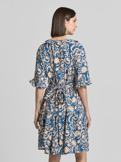 Frauenmodel trägt Knielanges Kleid aus Viskose im Allover-Look von Christian Berg Woman in A-Linie mit Bindegürtel, Volants, V-Ausschnitt, gemustert in Blau und Beige, feine glatte Textur, Rückenlänge 100 cm, Ganzkörperansicht Rückansicht.