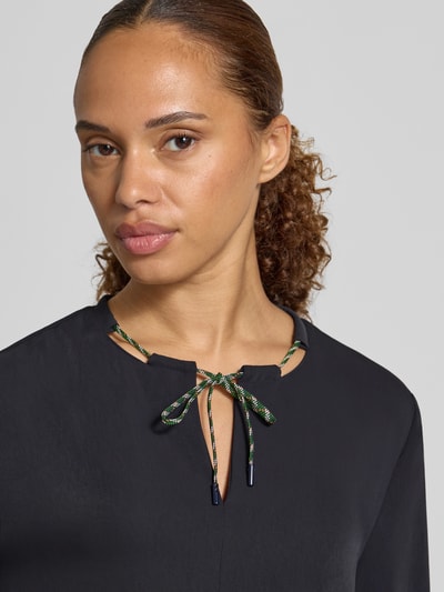 Kobiece modelka nosi Relaxed Fit Bluse mit Tunnelzug od Marc Cain, dekolt w serek, tunel, rękawy z elastycznym wykończeniem, bluzka z długim rękawem, kolor czarny, długość tyłu w rozmiarze 36: 61 cm, długość rękawa: 62 cm, zbliżenie na górną część ciała.