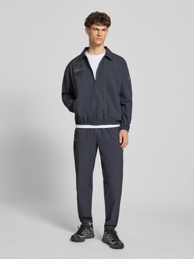 Männermodel trägt Regular-Fit Hemdjacke mit Logo Modell 'HALO MOVE' von HALO in Dunkelgrau mit Umlegekragen und Reißverschluss, Ganzkörperansicht von vorne. Rückenlänge bei Größe M: 66 cm, Ärmellänge bei Größe M: 61 cm.