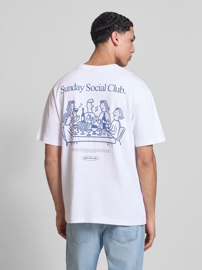 Männermodel trägt Relaxed Fit T-Shirt aus reiner Baumwolle Modell 'FRED DU MARTIN' von Only & Sons in Weiß mit blauem Motiv-Print, Feinripp, Ganzkörperansicht Rückansicht.