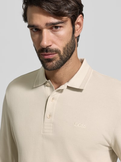 Męski model nosi Koszulkę polo Regular Fit z czystej bawełny Model 'PLISY' od BOSS Green, jednokolorowa, wyhaftowane logo, dekolt henley, długi rękaw, materiał pika, zbliżenie na górną część ciała.