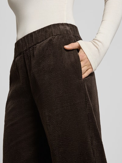 Frauenmodel trägt Relaxed Fit Cordhose aus reiner Baumwolle von Marc O'Polo Denim, dunkelbraun, elastischer Bund, strukturierte Cord-Oberfläche, seitliche Eingrifftasche, Nahaufnahme Oberkörper.