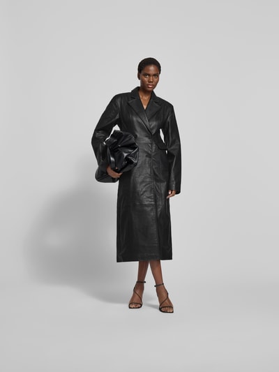 Frauenmodel trägt Mantel aus echtem Lammleder von ROTATE in Schwarz, taillierte Passform, Reverskragen, doppelte Knopfleiste, Taschen mit Überschlag, Rückenlänge 128 cm, Brustweite 46 cm, Ärmellänge 68 cm, Ganzkörperansicht von vorne.