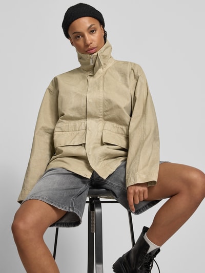 Frauenmodel trägt Jacke aus reiner Baumwolle mit Kapuze von Victoria Beckham in Beige, lockere Passform, seitliche Eingrifftaschen, durchgehende Reißverschluss und Knopfleiste, Rückenlänge 67 cm, Brustweite 74 cm, Ärmellänge 56 cm, Ganzkörperansicht von vorne.
