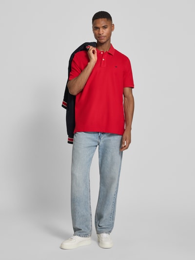 Männermodel trägt Regular Fit Poloshirt mit Logo-Stitching von Fynch-Hatton aus Reine Baumwolle in Rot, Polokragen, Ganzkörperansicht von vorne. Herren Modell, Rückenlänge bei Größe M: 70 cm, Kurzärmeliges Design, kombiniert mit hellblauer Jeans und weißen Sneakern.