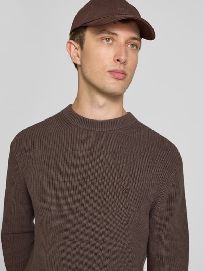 Männermodel trägt Slim Fit Pullover aus reiner Baumwolle in Strick-Optik von Replay, braun, feine Struktur, Logo-Stitching, Nahaufnahme Oberkörper.