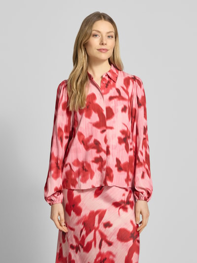 Frauenmodel trägt Regular Fit Hemdbluse aus reiner Viskose Modell 'Asina' von YAS mit floraler Allover-Print, langärmelig, Hemdblusenkragen, elastische Ärmelabschlüsse, bunte Rottöne auf strukturiertem Stoff, Ganzkörperansicht von vorne.