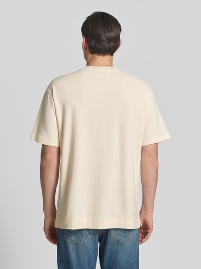 Männermodel trägt Relaxed Fit T-Shirt aus reiner Bio-Baumwolle Modell 'MAARKOS WAFFLE' von Armedangels in Creme mit Waffle-Struktur, unifarben, Logo-Stitching, Kurzarm, Rundhals, Feinstrick, Ganzkörperansicht Rückansicht.