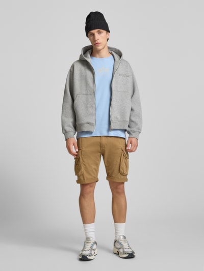 Männermodel trägt T-Shirt mit Logo und Rundhalsausschnitt von Alpha Industries, Herren T-Shirt aus Reine Baumwolle, Regular-Fit, Logo, hellblau, Rückenlänge bei Größe M 67 cm, Ganzkörperansicht von vorne.