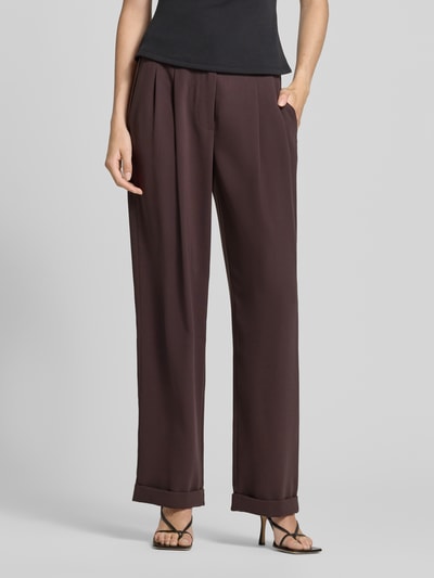 Frauenmodel trägt Relaxed Fit Stoffhose mit Kellerfalten von Armani Exchange in Dunkelbraun, glatte Oberfläche, Eingriff- und Gesäßtaschen, umgeschlagene Beinabschlüsse, Knopf- und Reißverschluss, Ganzkörperansicht von vorne.
