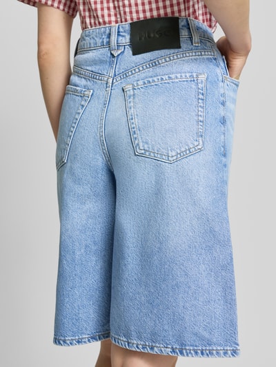 Kobiece model prezentuje Wide Fit Shorts aus reiner Baumwolle Modell 'GELITA_1' od HUGO, denimowy wygląd, wysoki stan, 5 kieszeni, łatka z logo, bawełniany materiał, widok całej sylwetki z tyłu.