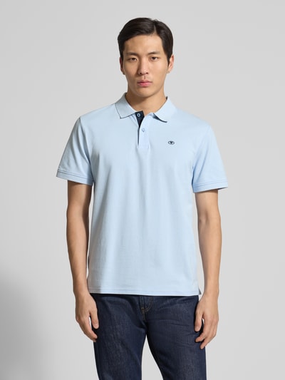 Männermodel trägt Regular Fit Poloshirt aus reiner Baumwolle von Tom Tailor, hellblau, kurzarm, Piqué-Struktur, Logostick, V-Ausschnitt, Ganzkörperansicht von vorne.