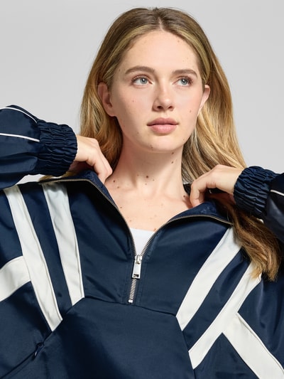 Modelka kobieca nosi Regular Fit Anorak mit Viskose-Anteil Modell 'Bicca' od Gestuz, granatowe i białe kolory, krój regular fit, materiał elastyczny, stójka z zamkiem, kieszenie na zamek, elastyczne mankiety, Nahaufnahme górnej części ciała. Szerokość w rozmiarze 36: 55 cm, długość z tyłu: 60 cm, szerokość w biuście: 69 cm, długość rękawa: 65 cm.
