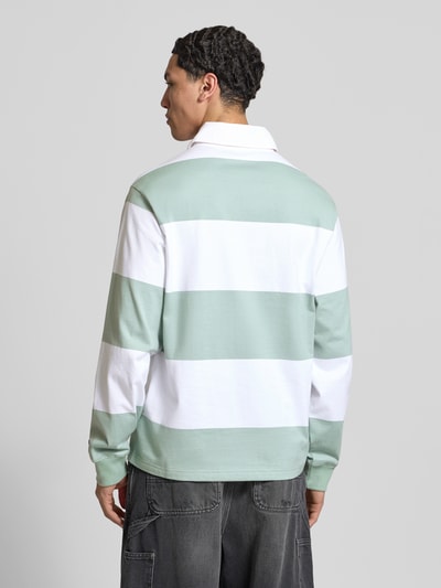 Männermodel trägt Relaxed Fit Poloshirt aus Baumwolle von CHAMPION mit breiten grünen und weißen Streifen, Rückenansicht, Ganzkörperansicht Rückansicht