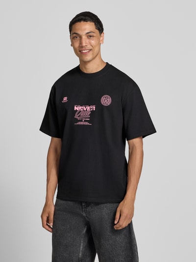 Männermodel trägt T-Shirt mit Statement-Print und Rundhalsausschnitt von Redefined Rebel aus Baumwoll-Mix, Relaxed-Fit, Modell 'Bruno', Rückenlänge 70 cm, schwarze Farbe, Ganzkörperansicht von vorne.