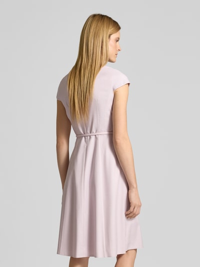 Frauenmodel trägt Knielanges Kleid mit Gürtel von Christian Berg Woman Selection, Material-Mix mit Viskose-Anteil, fein strukturiert, A-Linie, pastellrosa Ton, V-Ausschnitt, Gürtel, Knielänge, Ganzkörperansicht Rückansicht.