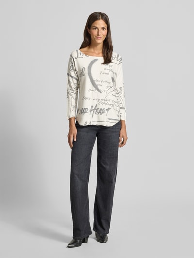 Frauenmodel trägt Longsleeve mit 3/4- Arm und Statement-Print von ZABAIONE, weiß mit grauen Schriftzügen, Rundhalsausschnitt, Ganzkörperansicht von vorne.