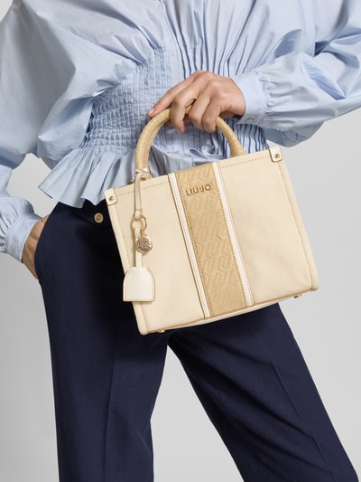 Frauenmodel trägt Handtasche mit Label-Applikation Modell 'RIDHI' von Liu Jo White aus Reine Baumwolle mit Hauptfach und Reißverschluss, Tragehenkel und Schulterriemen, Breite 25 cm, Länge 20 cm, Tiefe 10 cm, Länge Schulterriemen 30 cm, Nahaufnahme Oberkörper.