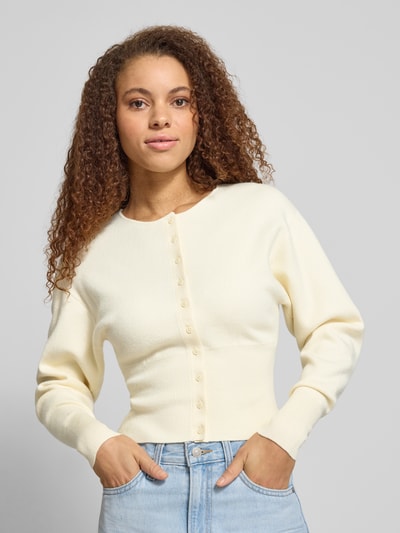 Modelka nosi Slim Fit Cardigan aus Viskose-Mix von Gina Tricot w kolorze kremowym, krój regular fit, dzianinowa faktura, długie rękawy, zapięcie na guziki, szerokie i elastyczne mankiety, długość tyłu w rozmiarze S 48 cm, długość rękawa 59 cm, widok na górną część ciała z przodu.