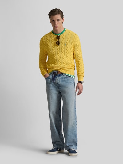 Męski model nosi Regular Fit Strickpullover aus reiner Baumwolle od Polo Ralph Lauren, żółty sweter w warkoczowy wzór, crew neck, dżinsy, widok całej sylwetki z przodu.