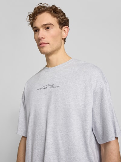 Männermodel trägt T-Shirt mit Label-Print und Rundhalsausschnitt von HALO in Hellgrau, reine Baumwolle, Boxy Fit, Nahaufnahme Oberkörper.