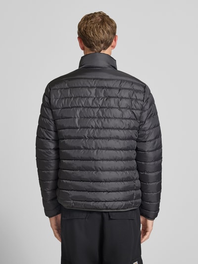 Männermodel trägt dunkelgraue, gesteppt strukturierte Jacke mit Label-Patch Modell 'ELVIS' von JACK & JONES, Ganzkörperansicht Rückansicht. Gerader Schnitt, Stehkragen, Reißverschluss, seitliche Reißverschlusstaschen, Maße laut Kontext.