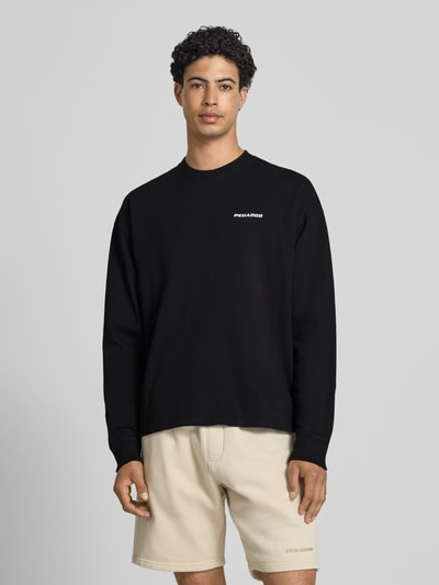 Männermodel trägt Oversized Sweatshirt mit Logo-Stitching Modell 'Rusk' von Pegador in Schwarz aus Reine Baumwolle, Oversized-Fit, Ganzkörperansicht von vorne. Rückenlänge bei Größe M: 61 cm.